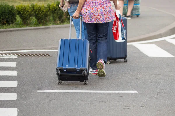 Женщина в разноцветной одежде с голубым чемоданом, переходящей дорогу — стоковое фото