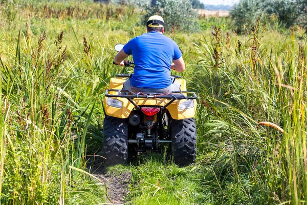 Kaukasischer Mann mit Sportschutzbrille auf einem Geländequad über unwegsames Gelände zwischen hohen Grasbüschen. Abenteueraktivitätskonzept — Stockfoto