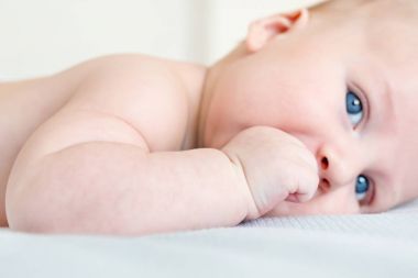 Bir yatakta yatarken çocuk portresi. Sağlıklı çocuk yumruğunu emme close-up. Arka plan bulanık yumrukla odaklanmak. Bebek diş çıkarma kavramı