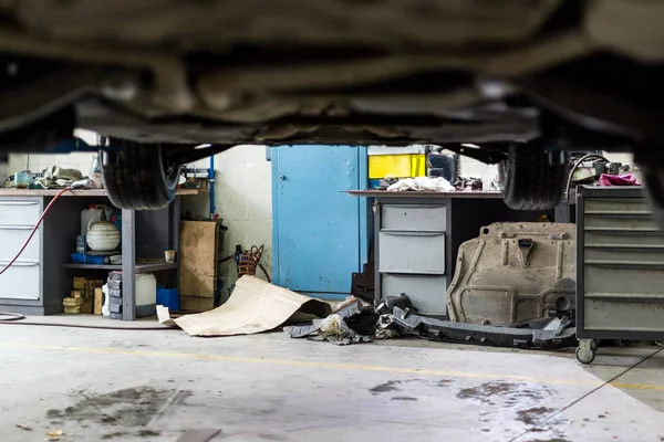 Macchina appesa all'ascensore alla stazione di Sevice. Centro di manutenzione del veicolo sporco. Disturbo, fango, macchie e caos. officina automobilistica maldestra non professionale — Foto Stock