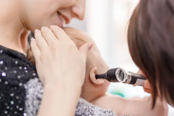 医生用耳镜检查孩子的耳朵。妈妈用手抱着孩子。儿童保健与疾病预防概念 — 图库照片