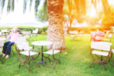 Cafe ile yeşil çim çim, palmiye ağaçları, masa ve sandalyeler ziyaretçiler için deniz kıyısında. Bulanık