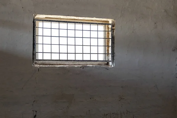 Ancien mur blanc avec fenêtre recouverte d'une grille de fer. Le soleil brille à travers le gril. Intérieur de la prison. Concept d'illumination. Espace de copie — Photo
