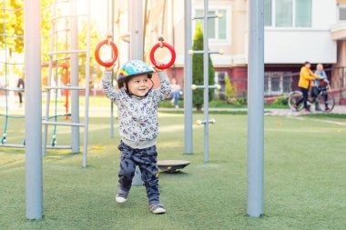 Sevimli, tapılası küçük çocuk, açık apartmandaki spor sahasında jimnastik yüzükleriyle sallanmayı seviyor. Dışarıda aletlerle oynayıp egzersiz yapan mutlu bir çocuk. Sağlıklı