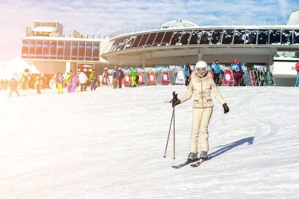 Porträtt av ung vuxen vacker glad kaukasisk kvinna ler nära liftstationen på alpin vinterskidort. Flicka i modedräkt, goggles och vit hjälm. Vintersport semester och turism — Stockfoto