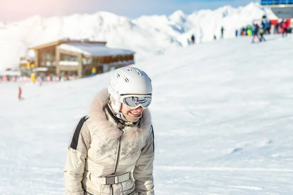 Porträtt av ung vuxen vacker glad kaukasisk kvinna ler nära liftstationen på alpin vinterskidort. Flicka i modedräkt, goggles och vit hjälm. Vintersport semester och turism — Stockfoto