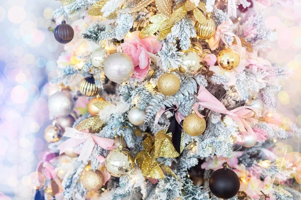 Close-up shiny pink gold decorated Christmas tree with lights ribbons, baubles and balls at house indoors. Xmas decoration background. Winter holidays card. Toned with bright bokeh lights