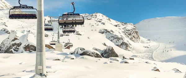 Teleférico de telesilla en la montaña montañosa alpina estación de invierno en un día soleado brillante. Telesilla telesilla de cable con la gente disfruta del esquí y snowboarding.Banner panorámica amplia vista de las pistas cuesta abajo — Foto de Stock