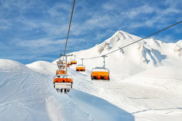 Skilift kabelbaan op heuvelland alpine berg wintersportplaats op heldere zonnige dag. Ski stoeltjeslift kabelbaan met mensen genieten van skiën en snowboarden.Banner panoramisch wijds uitzicht op afdalingen — Stockfoto