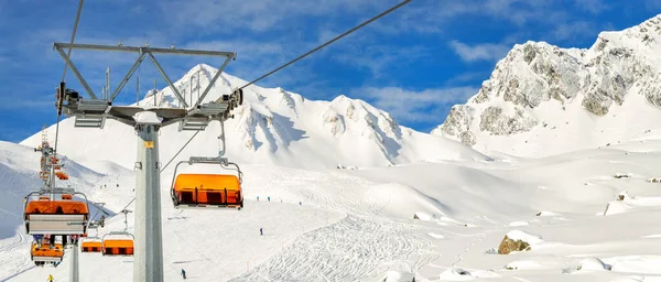 Teleférico de telesilla en la montaña montañosa alpina estación de invierno en un día soleado brillante. Telesilla telesilla de cable con la gente disfruta del esquí y snowboarding.Banner panorámica amplia vista de las pistas cuesta abajo — Foto de Stock