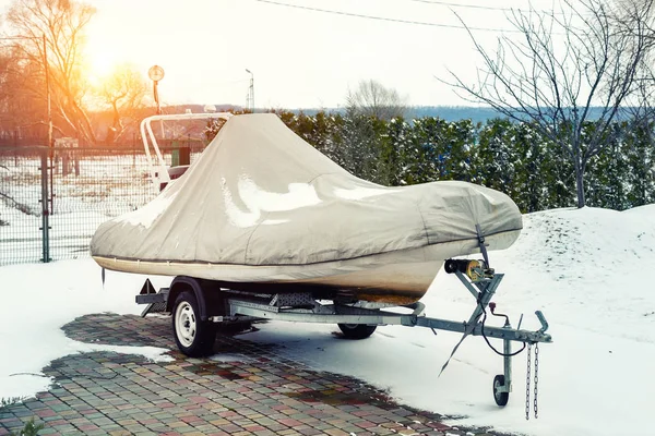 Felfújható luxus halászmotorcsónak fedett álló pótkocsi a téli időszakban szezonális tárolás a kertben. Zsugorfóliába csomagolt hajó, parkolóban telelve — Stock Fotó