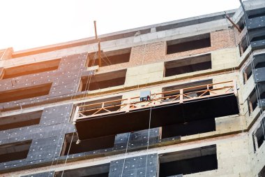 Yüksek kule yerleşim binasının duvarının yanında izolasyon ve inşaat alanında havalandırmalı ön cephe bulunan askıya alınmış bir yapı beşiği. Mühendislik şehir geçmişi