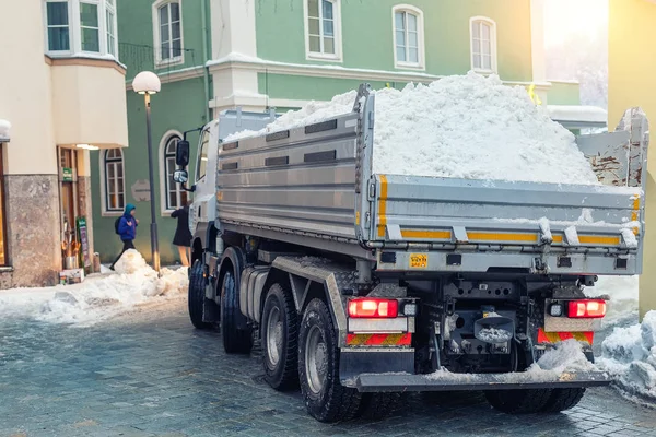 Grande autocarro ribaltabile completamente carico di neve che attraversa la stretta strada del centro storico nella vecchia città europea. Rimozione neve macchinari pesanti. Servizi comunali pulizia e manutenzione strade cittadine — Foto Stock