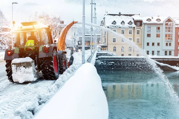 Nehéz önkormányzati szolgáltatások gépek, amelyek eltávolítják a havat a város utcáiról. Nagy traktor hófúvó hófúvó a hídfőútról a folyóra. Az utcák tisztítása és hóesés utáni hóeltakarítás a téli szezonban — Stock Fotó