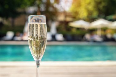 Tatil sırasında lüks tatil otelinde havuz kenarına karşı yakın çekim beyaz şampanya veya prosecco cam. Açık mavi havuz arka plan ile yükselen kabarcıklar ile köpüklü şarap. Ferahlatıcı alkol içeceği