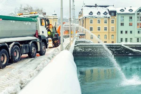 Maquinaria pesada de servicios municipales quitando nieve de las calles de la ciudad. Soplador de nieve tractor grande que sopla nieve desde el camino del puente en el río. Limpieza de calles y remoción de nieve después de nevadas en invierno —  Fotos de Stock