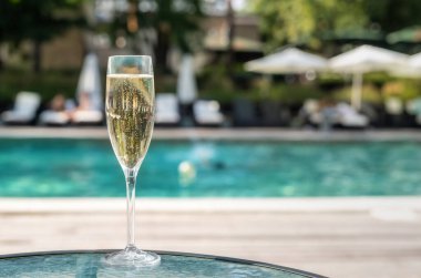 Tatil sırasında lüks tatil otelinde havuz kenarına karşı yakın çekim beyaz şampanya veya prosecco cam. Açık mavi havuz arka plan ile yükselen kabarcıklar ile köpüklü şarap. Ferahlatıcı alkol içeceği