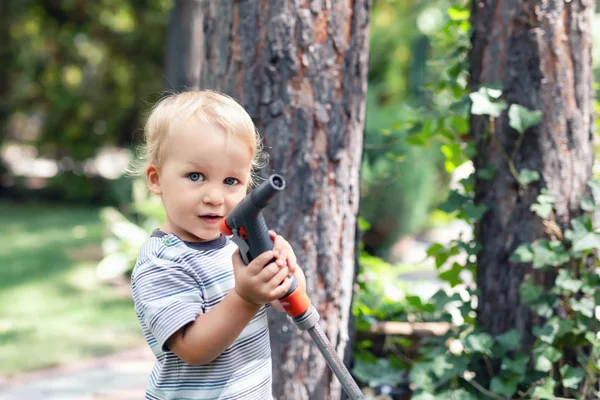 Aranyos, imádnivaló, fehér, szőke fiú, aki locsolóval locsolja a kertet. Gyermek kis segítő játszik kertészkedés nyáron a szabadban — Stock Fotó