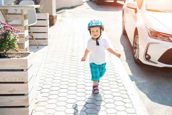 可爱的白种人，金发碧眼的男孩儿，戴着头盔走在城市街道上，在阳光灿烂的夏日早晨骑自行车骑摩托车。 有趣的小孩喜欢户外活动. 积极的生活方式 — 图库照片