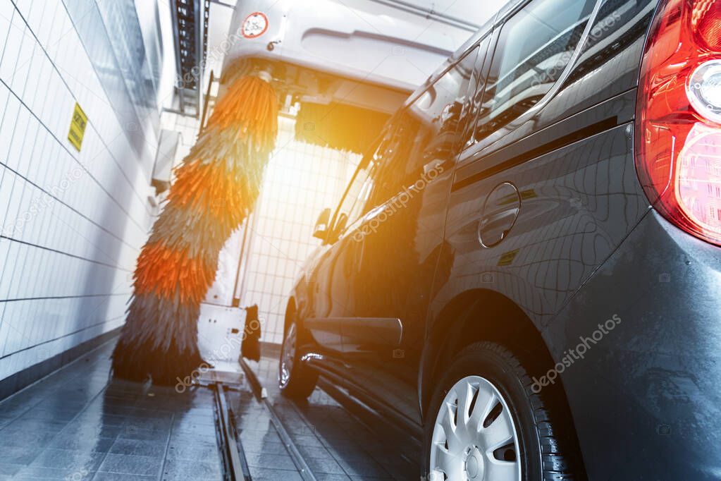 Black modern delivery minivan car cleaning with robot automatic tunnel car wash machine. Grey and red soft brushes washing vehicle with foam at gas petrol service cleaner station. Carwash business