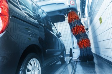 Robot otomatik tünel oto yıkama makinesiyle siyah, modern minibüs araba temizliği. Benzin istasyonunda köpükle yıkanan gri ve kırmızı fırçalar. Araba yıkama işi.