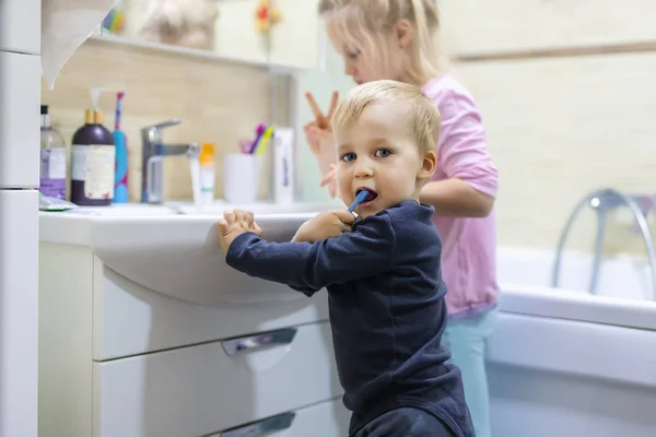 Dwoje uroczych blond, białych rodzeństwa myjących twarz i czyszczących zęby szczoteczką do zębów w łazience w domu rano. Małe dzieci brat i siostra robią codziennie higyene opieki zdrowotnej. Zabawne dzieciaki. — Zdjęcie stockowe