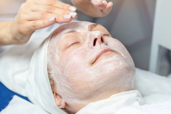 Крупним планом руки косметолога роблять процедури проти віку, масаж обличчя та голови для жіночого клієнта середнього віку в клініці краси. Косметолог робить лікування шкірного покриву. — стокове фото