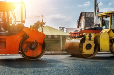 Asphalt Higway yolu şantiyesi. Yol işlerinde ağır endüstriyel makineler ve mavi gökyüzü arka planda. Buharlı yol silindiri, kaldırım makinesi ve bahşiş kamyonu yeni kaldırım için sıcak zift boşaltıyor..