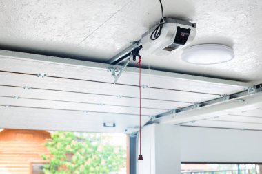 Açma kapısı ve otomatik garaj kapısı açacağı. Acil durum kablosu ile tavana monte edilmiş elektrikli motor teçhizatı. Çift kişilik boş bir garaj. Giriş kapısı da açık..
