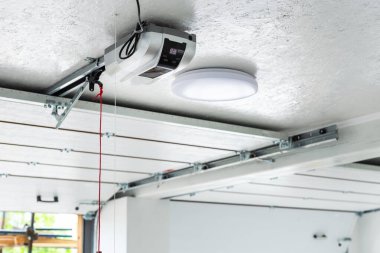 Açma kapısı ve otomatik garaj kapısı açacağı. Acil durum kablosu ile tavana monte edilmiş elektrikli motor teçhizatı. Çift kişilik boş bir garaj. Giriş kapısı da açık..