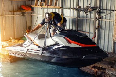 Son sınıf öğrencisi modern jet ski 'yi suya indiriyor ya da kaldırıyor. Kuru depo için tel vinçle asılıydı. Botlar ve jet-ski depolama, servis ve bakım için tekne garajı.