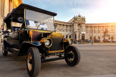Arka planda mavi gün batımı gökyüzüne sahip Viyana Hofburg Sarayı 'na karşı turistik şehir turnesi için klasik eski model golf aracı olarak tanımlanamayan elektrikli golf arabası görmek. Avusturya seyahati ve turizm konsepti..