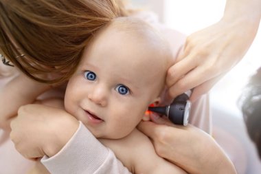 Doktor Pediatrist otoskopla çocuğun kulağını inceliyor. Anne elleriyle bebeği tutuyor. Tıp, sağlık, pediatri ve insanlar. Çocuk sağlığı ve hastalık önleme kavramı .