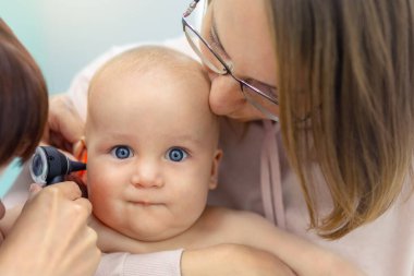 Doktor Pediatrist otoskopla çocuğun kulağını inceliyor. Anne elleriyle bebeği tutuyor. Tıp, sağlık, pediatri ve insanlar. Çocuk sağlığı ve hastalık önleme kavramı .