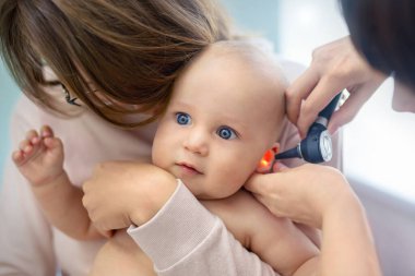 Doktor Pediatrist otoskopla çocuğun kulağını inceliyor. Anne elleriyle bebeği tutuyor. Tıp, sağlık, pediatri ve insanlar. Çocuk sağlığı ve hastalık önleme kavramı .