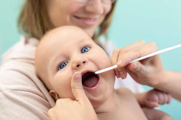 小児科医は子供の喉と歯を調べる 健康診断をしながら手で赤ちゃんを抱えるお母さん 小児科 子どもの健康と疾病予防の概念 — ストック写真