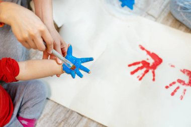 Sevimli, beyaz, sarışın küçük kardeşler anneleriyle evde fırça ve avuç içi boyama yaparken eğleniyorlar. Neşeli mutlu çocuklar resim çizerek gülümsüyor..