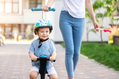 Küçük sevimli beyaz çocuk kasklı portresi. Şehir parkında üç tekerlekli dengeli motosiklet sürerken eğleniyor. Önce çocuk bisikleti. Çocuk açık hava spor aktiviteleri.