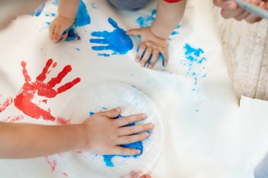 Sevimli, beyaz, sarışın küçük kardeşler anneleriyle evde fırça ve avuç içi boyama yaparken eğleniyorlar. Neşeli mutlu çocuklar resim çizerek gülümsüyor..