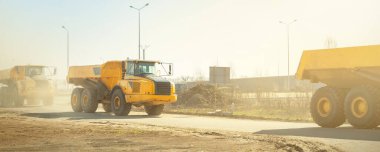 Birçok büyük eklemli ağır endüstriyel sarı damperli kamyonlar güneşli bir günde mavi gökyüzü arka planına sahip yeni otoyol şantiyesinde yol alıyorlar. Açık çukur üzerinde çalışan inşaat ekipmanı makineleri.