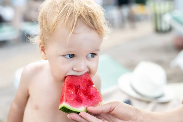 妈妈在海上或海滨度假时喂可爱可爱的高加索金发碧眼的小男孩一片新鲜甜甜甜的西瓜 孩子们中午从妈妈手里咬着多汁的浆果点心吃午饭 — 图库照片