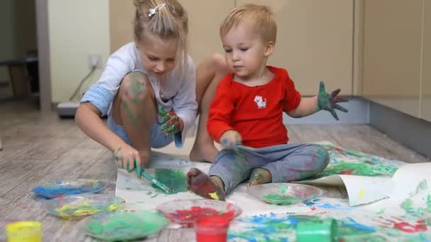 Adorables lindos hermanos rubios caucásicos pequeños niños disfrutan divirtiéndose junto con la madre pintando pincel y la palma en casa en interiores. Alegre feliz niños sonriendo dibujo obra maestra arte imagen — Vídeo de stock