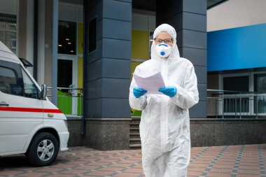 Yüz maskesi takan yorgun kadın doktor, bilim adamı ya da hemşire portresi ve dışarıda kimi tedavi ettiğini gösteren biyolojik tehlikeli madde kıyafeti. Coronavirus covid-19 salgını tehlikesi.