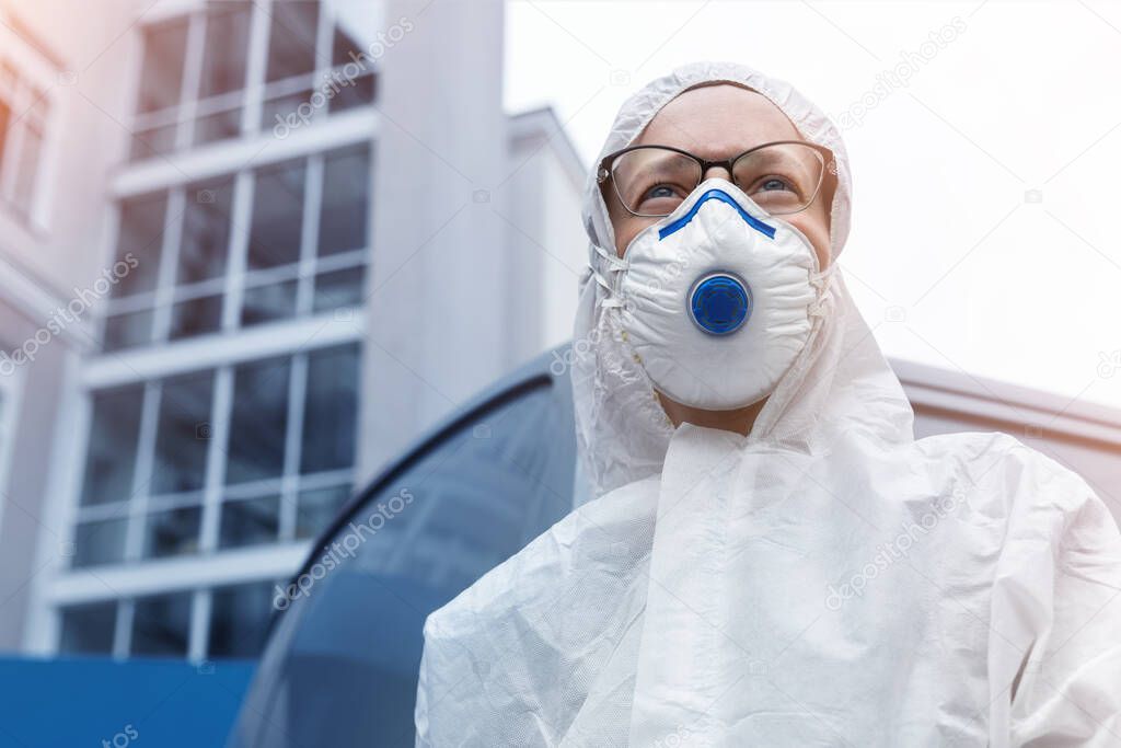 Portrait of tired exhausted pensive female doctor, scientist or nurse wearing face mask and biological hazmat ppe suit looking forwad with anxious aware outdoor. Coronavirus covid-19 outbreak danger.