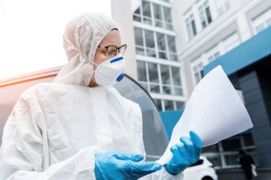 Yüz maskesi takan yorgun kadın doktor, bilim adamı ya da hemşire portresi ve dışarıda kimi tedavi ettiğini gösteren biyolojik tehlikeli madde kıyafeti. Coronavirus covid-19 salgını tehlikesi.