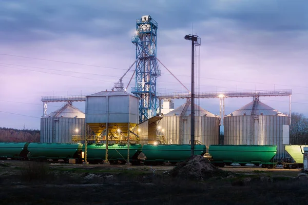 Armazém de armazenamento de cereais de silos de grãos agrícolas de aço moderno que carrega o transporte ferroviário de carga à noite ou ao nascer do sol. Atribuição de terras agrícolas paisagem da indústria rural. Instalação da loja de moinhos — Fotografia de Stock