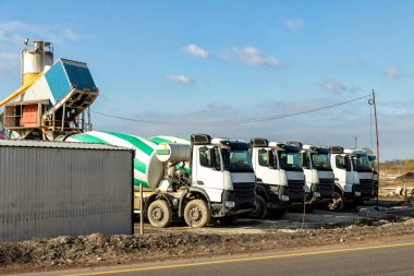 Yeni asfalt yol inşaatında, taşınabilir beton fabrikasına karşı park etmiş birçok modern büyük mikser kamyonları. Ağır makineler ve endüstriyel tesisler