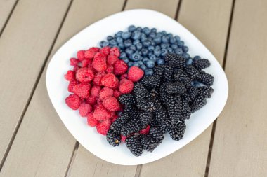 Atıştırmak için çeşitli tatlı, organik mevsimlik meyveli beyaz seramik tabak. Kahvaltı için taze ahududu, böğürtlen ve yaban mersini karışımı. Sağlıklı vitamin beslenme diyeti