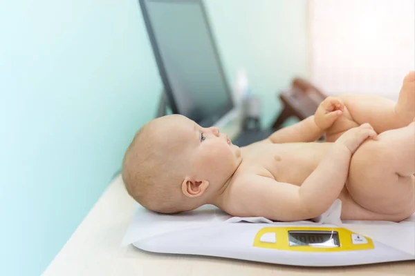 Pediatrician specialist taking measurement infant child weight during screening examination. Cute caucasian baby lying on electronic scales doctors office. Children healthcare and disease prevention