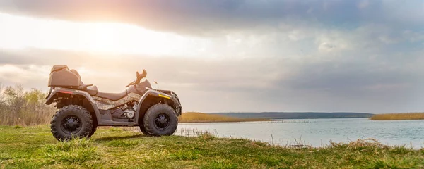 ATV awd quadbike motocykl pov pohled v blízkosti jezera nebo řeky rybník pobřeží s krásnou přírodou krajiny a oblačnosti nebe pozadí. Offroad dobrodružství výlet. Extrémní sportovní aktivity panoranic široký pohled — Stock fotografie